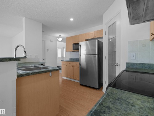 Kitchen featuring wood-finish cabinetry, stainless steel appliances, a double basin sink with a high-arc faucet, and green countertops - 2410 32B Street Nw, Edmonton, AB 