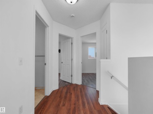 Hallway featuring wood-finish flooring, white walls, and a staircase with a white handrail - 2410 32B Street Nw, Edmonton, AB 