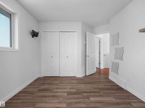 Wood-finish flooring, white bi-fold closet doors, white interior doors, and a window with white trim - 2410 32B Street Nw, Edmonton, AB 