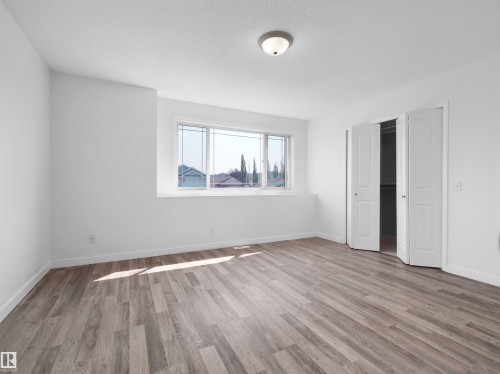 Wood-finish flooring, white walls, flush mount ceiling light, bi-fold closet doors, and a multi-pane window - 2410 32B Street Nw, Edmonton, AB 
