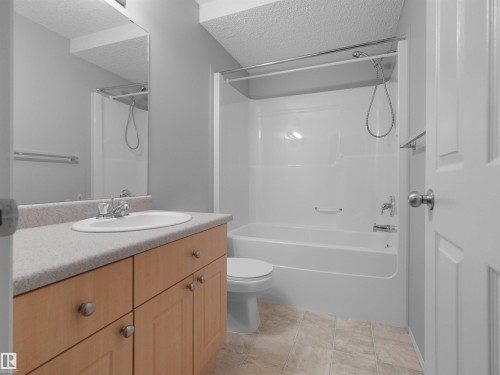 Bathroom featuring a full vanity with wood-finish cabinetry, a single basin sink, and a combination tub and shower - 2410 32B Street Nw, Edmonton, AB 