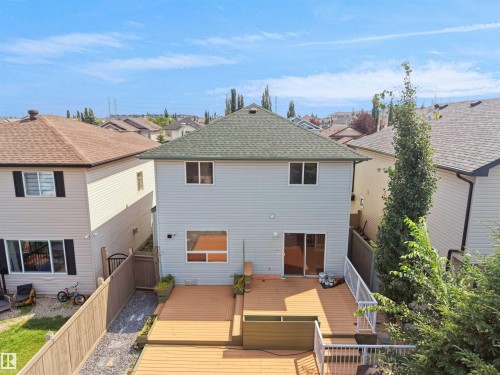 Multi-level wood deck with white railings, featuring sliding glass door access, and a gravel pathway alongside the property - 2410 32B Street Nw, Edmonton, AB 