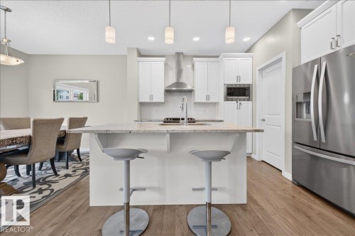 Modern kitchen featuring a central island with countertop seating, white cabinetry, stainless steel appliances, and wood-finish flooring - 2709 Collins Crescent Sw Sw, Edmonton, AB - Indoor Photo Showing Kitchen With Stainless Steel Kitchen With Upgraded Kitchen