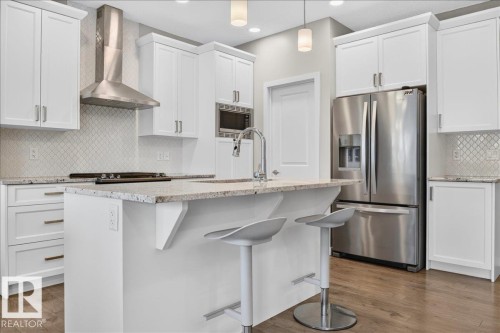 Kitchen featuring white shaker cabinetry, stainless steel appliances, a center island with bar seating, a tile backsplash, and light wood-finish flooring - 2709 Collins Crescent Sw Sw, Edmonton, AB - Indoor Photo Showing Kitchen With Stainless Steel Kitchen With Upgraded Kitchen