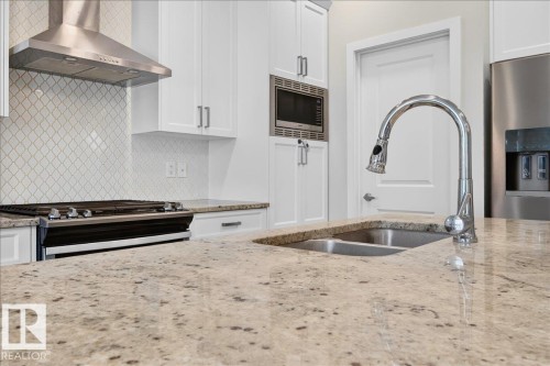 Kitchen featuring granite countertops, white cabinetry, a stainless steel range hood, a tiled backsplash, and a double basin sink with a chrome faucet - 2709 Collins Crescent Sw Sw, Edmonton, AB - Indoor Photo Showing Kitchen With Stainless Steel Kitchen With Double Sink With Upgraded Kitchen