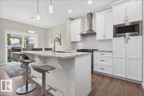 Modern kitchen featuring white cabinetry, granite countertops, a built-in microwave, stainless steel range hood, and wood-finish flooring - 2709 Collins Crescent Sw Sw, Edmonton, AB - Indoor Photo Showing Kitchen With Upgraded Kitchen