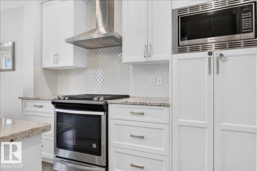 Contemporary kitchen featuring a stainless steel range, coordinating range hood, built-in microwave, white shaker cabinetry, and light-toned granite countertops - 2709 Collins Crescent Sw Sw, Edmonton, AB - Indoor Photo Showing Kitchen With Upgraded Kitchen