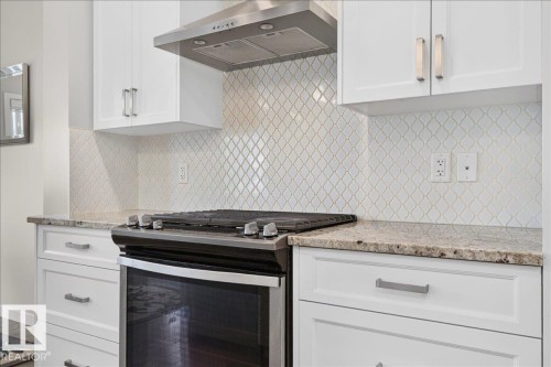 Kitchen featuring a gas range, stainless steel range hood, white shaker-style cabinetry, patterned tile backsplash, and stone countertops - 2709 Collins Crescent Sw Sw, Edmonton, AB - Indoor Photo Showing Kitchen With Upgraded Kitchen