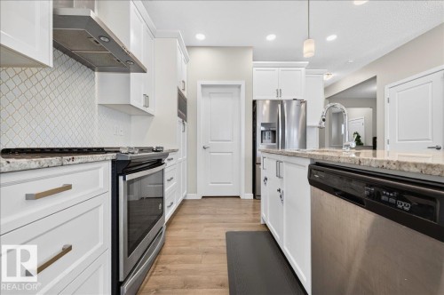 Kitchen featuring white cabinetry, stainless steel appliances, granite countertops, a decorative tile backsplash, and wood-finish flooring - 2709 Collins Crescent Sw Sw, Edmonton, AB - Indoor Photo Showing Kitchen With Stainless Steel Kitchen With Upgraded Kitchen