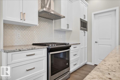 Contemporary kitchen featuring white cabinetry, light-toned countertops, patterned backsplash, stainless steel range with overhead hood, and dark wood-finish flooring - 2709 Collins Crescent Sw Sw, Edmonton, AB - Indoor Photo Showing Kitchen With Upgraded Kitchen
