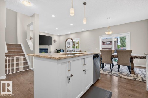Kitchen island featuring a granite-style countertop, undermount sink with a high-arc faucet, and white cabinetry - 2709 Collins Crescent Sw Sw, Edmonton, AB - Indoor Photo Showing Kitchen With Upgraded Kitchen