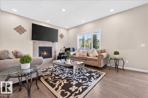 Living area featuring wood-finish flooring, a contemporary fireplace with a tiled surround, recessed lighting, and a large window - 2709 Collins Crescent Sw Sw, Edmonton, AB - Indoor Photo Showing Living Room With Fireplace