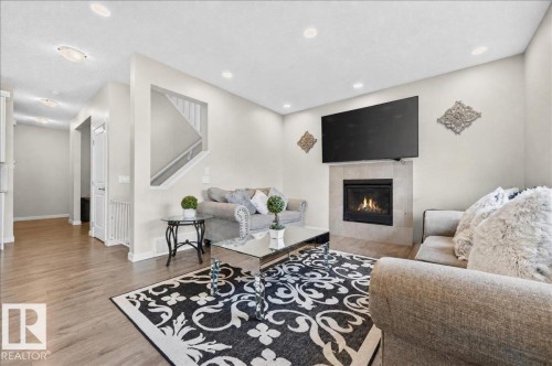 Living area featuring a gas fireplace with a tiled surround, wood-finish flooring, recessed lighting, and a partial view of a staircase with white railings - 2709 Collins Crescent Sw Sw, Edmonton, AB - Indoor Photo Showing Living Room With Fireplace
