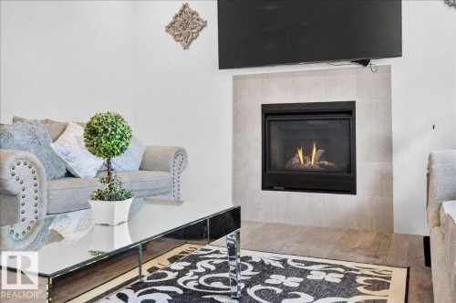 Living area featuring a modern fireplace with a light-toned tile surround and wood-finish flooring - 2709 Collins Crescent Sw Sw, Edmonton, AB - Indoor Photo Showing Living Room With Fireplace