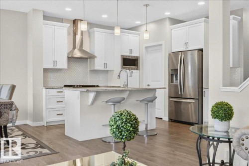 Kitchen featuring an island with seating, stainless steel appliances, white cabinetry, a tile backsplash, and light wood-finish flooring - 2709 Collins Crescent Sw Sw, Edmonton, AB - Indoor Photo Showing Kitchen With Upgraded Kitchen
