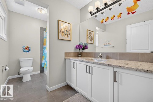 Bathroom featuring a vanity with a light-toned, speckled countertop, white cabinetry with dark hardware, a large mirror, a white toilet, and gray tile flooring - 2709 Collins Crescent Sw Sw, Edmonton, AB - Indoor Photo Showing Bathroom