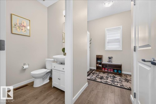 Powder room featuring a pedestal sink with white cabinetry, a toilet, and wood-finish flooring - 2709 Collins Crescent Sw Sw, Edmonton, AB - Indoor Photo Showing Bathroom