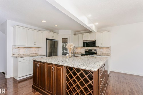 Kitchen featuring white upper cabinetry, a two-tiered island with built-in wine storage, granite countertops, and wood-finish flooring - 2407 Hagen Way Nw, Edmonton, AB 