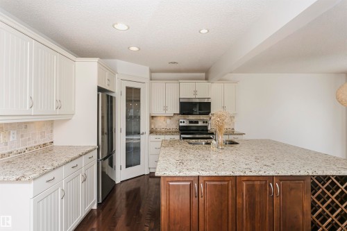 Kitchen featuring light-toned perimeter cabinetry, a dark wood-finish island with integrated wine storage, light-toned countertops, and a full suite of stainless steel appliances - 2407 Hagen Way Nw, Edmonton, AB 