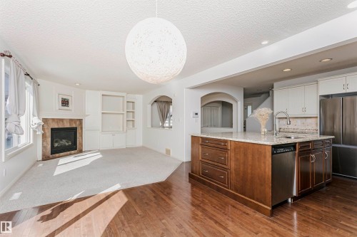 Wood-finish flooring leading to a built-in kitchen island with stone countertops and a stainless steel sink - 2407 Hagen Way Nw, Edmonton, AB 