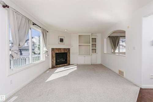 Recessed lighting, a gas fireplace with a tile surround, built-in cabinetry, an arched pass-through window, and light-toned carpeting - 2407 Hagen Way Nw, Edmonton, AB 