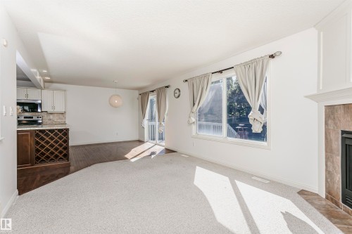 Open-concept living area featuring a built-in wine rack, wood-finish flooring, a contemporary pendant light fixture, and a white tile fireplace surround - 2407 Hagen Way Nw, Edmonton, AB 