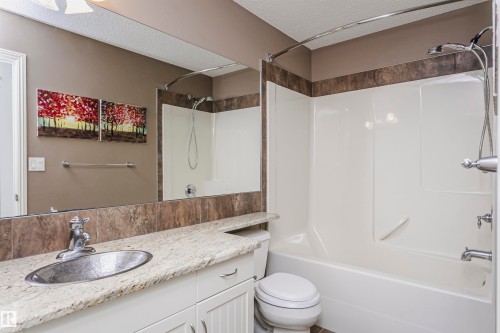 Bathroom featuring an integrated tub and shower with a curved shower rod, a vanity with a light-colored countertop, and a large wall-mounted mirror - 2407 Hagen Way Nw, Edmonton, AB 