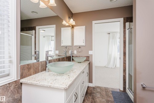 Dual vessel sinks with chrome faucets, white vanity with ample storage, light-toned granite countertop, and tiled flooring - 2407 Hagen Way Nw, Edmonton, AB 