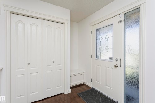 Entryway featuring wood-finish flooring, a white paneled entry door with decorative glass, a textured glass sidelight, and white paneled bi-fold closet doors - 2407 Hagen Way Nw, Edmonton, AB 