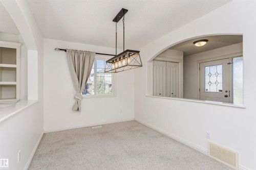 Recessed shelving, arched entryway, decorative glass panel door, light-colored carpeting, and a modern chandelier - 2407 Hagen Way Nw, Edmonton, AB 