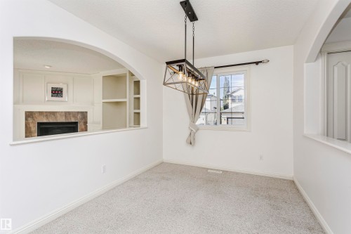 Archway opening to a fireplace with stone surround, built-in shelving, and wainscoting - 2407 Hagen Way Nw, Edmonton, AB 