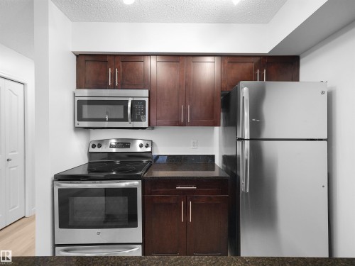 Full kitchen featuring stainless steel appliances, dark wood cabinetry, and stone countertops - #114 12035 22 Av Sw, Edmonton, AB 