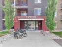 Building entrance featuring a concrete walkway, red exterior paneling, and a stone facade - #114 12035 22 Av Sw, Edmonton, AB 