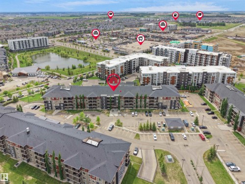 Aerial perspective showcasing multiple residential buildings, surface parking areas, and a central pond feature - #114 12035 22 Av Sw, Edmonton, AB 
