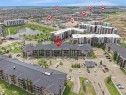 Aerial perspective showcasing multiple residential buildings, surface parking areas, and a central pond feature - #114 12035 22 Av Sw, Edmonton, AB 