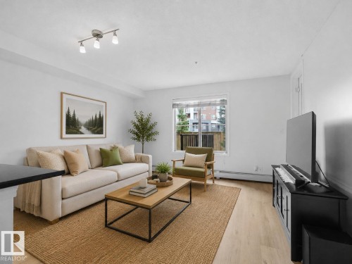 Bright living space featuring track lighting, large window with natural light, and light wood-finish flooring - #114 12035 22 Av Sw, Edmonton, AB 