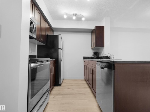 Wood-finish flooring, dark wood cabinetry, stainless steel appliances, dark countertops, and track lighting - #114 12035 22 Av Sw, Edmonton, AB 