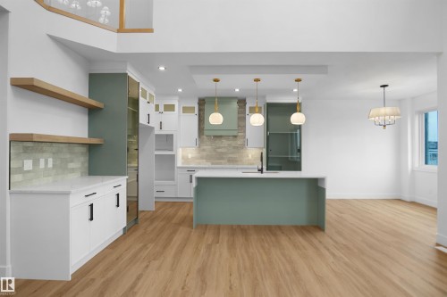Open-concept kitchen featuring an expansive island with a light green base, three pendant lights, and wood-finish flooring - 142 Edgewater Circle, Leduc, AB 