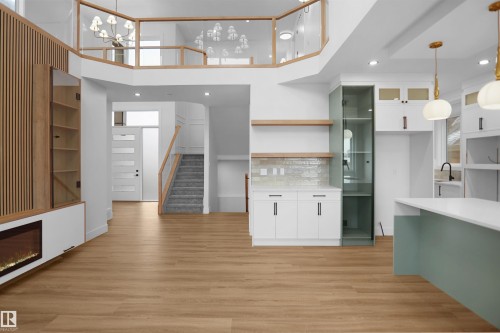 Open-concept living space with wood-finish flooring, a contemporary electric fireplace, a two-story ceiling, and a modern kitchen island with a white countertop - 142 Edgewater Circle, Leduc, AB 