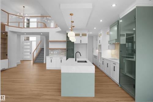 Open-concept kitchen featuring a center island with a light green base and a light-toned countertop, wood-finish flooring, white cabinetry with black hardware, recessed lighting, and a textured backsplash - 142 Edgewater Circle, Leduc, AB 