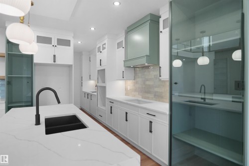Contemporary kitchen featuring a large island with a black undermount sink, white cabinetry with black hardware, and a sage green range hood - 142 Edgewater Circle, Leduc, AB 
