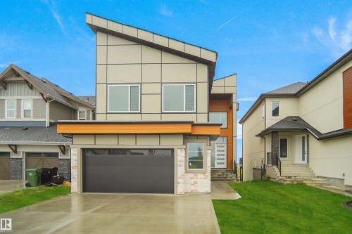 Modern architectural design featuring a multi-level facade, a dark gray garage door, white trim windows, a concrete driveway, and a front lawn. Landscaping artificially rendered. - 142 Edgewater Circle, Leduc, AB 