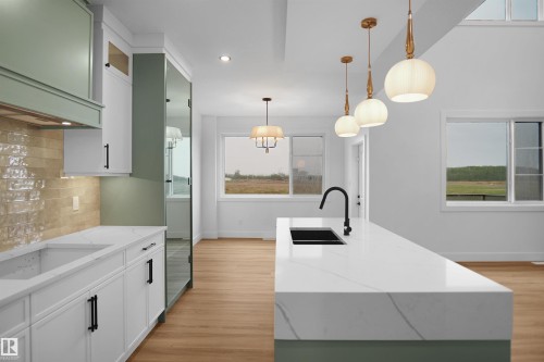 Open concept kitchen featuring a waterfall island with a black sink and faucet, pendant lighting, and two-tone cabinetry with a tiled backsplash - 142 Edgewater Circle, Leduc, AB 