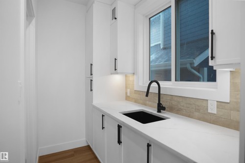Kitchenette featuring white cabinetry with matte black hardware, a solid surface countertop, an undermount sink with a black gooseneck faucet, and a tiled backsplash - 142 Edgewater Circle, Leduc, AB 
