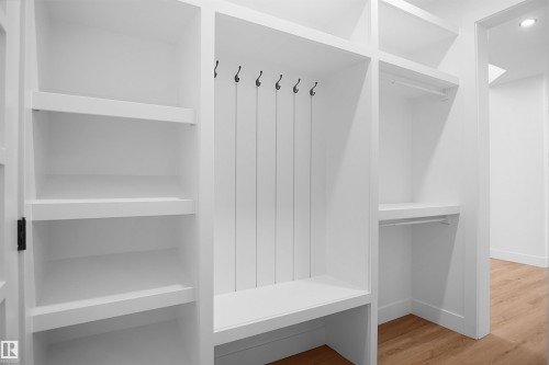 Built-in organizational system featuring white shelving, multiple hanging rods, black coat hooks, and a built-in bench - 142 Edgewater Circle, Leduc, AB 