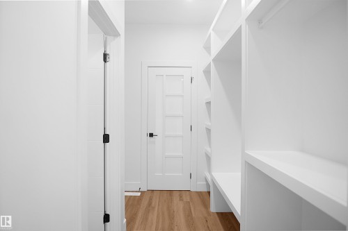 Walk-through closet with extensive built-in shelving, wood-finish flooring, white walls, and a five-lite interior door with matte black hardware - 142 Edgewater Circle, Leduc, AB 
