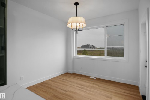 Spacious interior room featuring wood-finish flooring, white baseboards, and a large window with white trim - 142 Edgewater Circle, Leduc, AB 