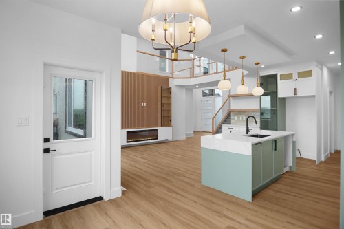 Open-concept living space featuring wood-finish flooring, a modern kitchen island with an integrated sink, a built-in electric fireplace below a media wall, and a multi-level design with glass railings - 142 Edgewater Circle, Leduc, AB 