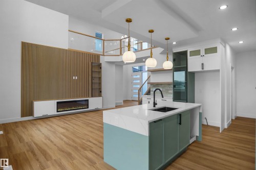 Open-concept interior featuring wood-finish flooring, a kitchen island with a white countertop and dark sink, and pendant lighting - 142 Edgewater Circle, Leduc, AB 