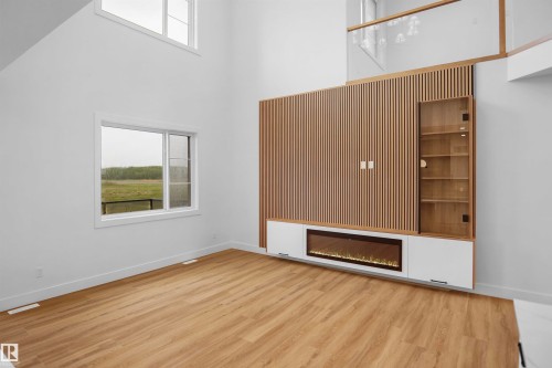 Integrated media center with wood-finish paneling, an electric fireplace, and built-in display shelving - 142 Edgewater Circle, Leduc, AB 